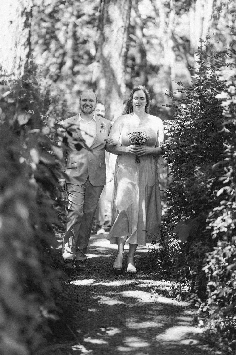 Black and white photo of a couple walking down a shaded garden path.
