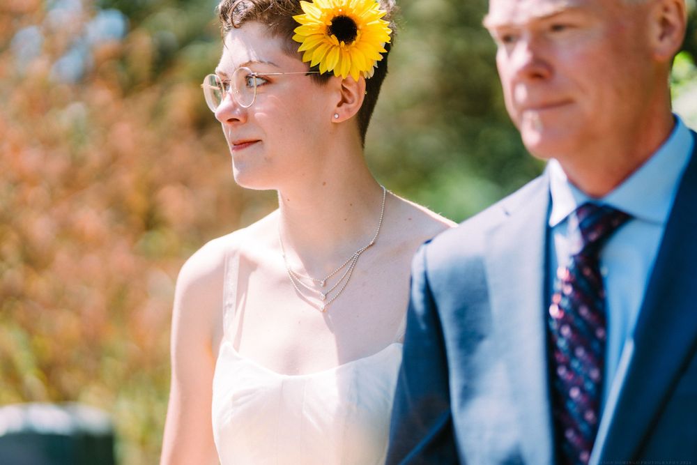 Person wearing a sunflower hair accessory standing next to someone in a navy suit.