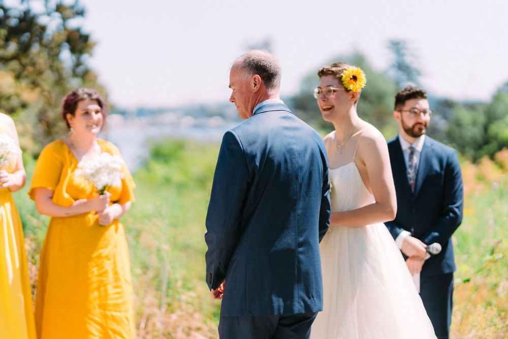 Outdoor wedding ceremony with attendants in yellow and white against a natural landscape.