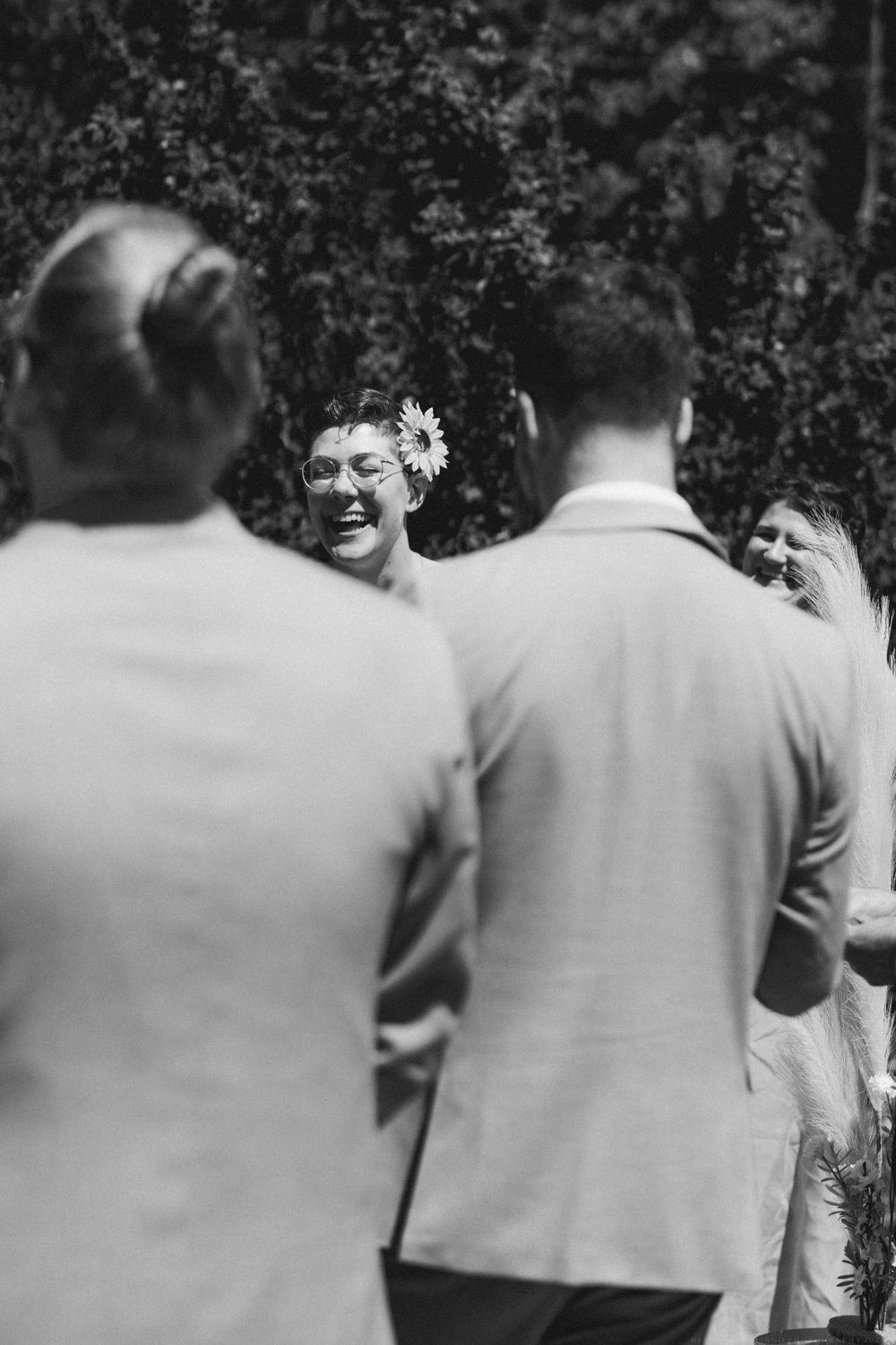 A black and white photo captures genuine laughter during an outdoor wedding ceremony.