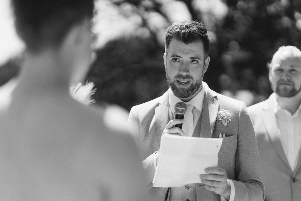 Black and white photo of groom reading wedding vows during outdoor ceremony.