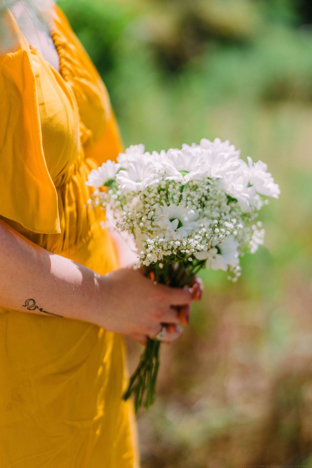 Person in yellow holding delicate white flower bouquet against blurred natural background.