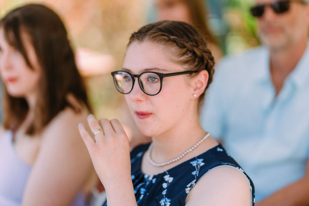 Guest in navy dress and glasses shows emotion during wedding celebration.