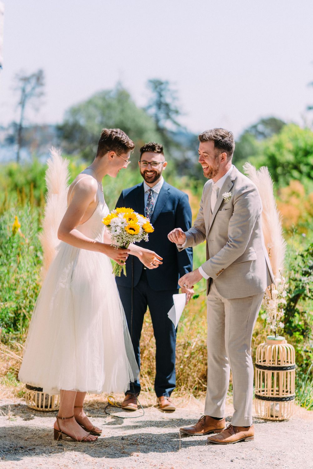 Three people share a joyful moment during outdoor wedding with yellow sunflowers and rustic decor.