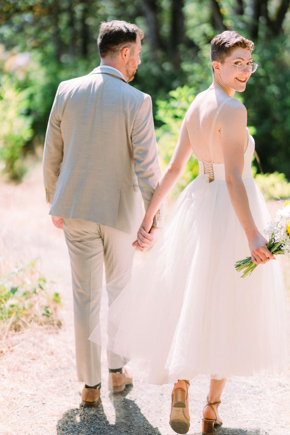 Couple holding hands while walking on garden path in wedding attire.