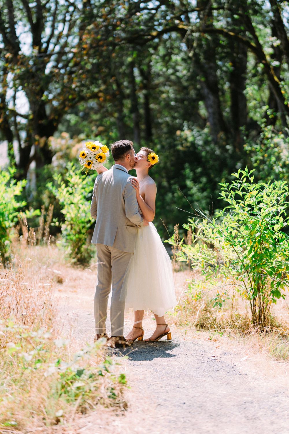 Romantic moment captured on garden path with sunflower bouquet and natural greenery.
