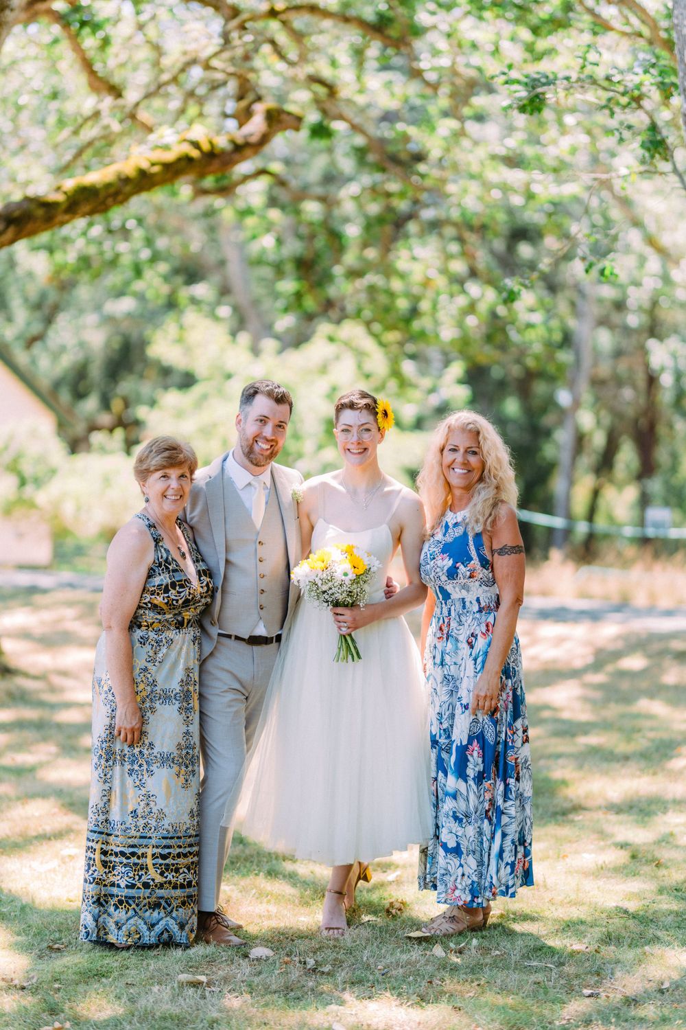 Small wedding group poses in sunlit garden with bride holding yellow bouquet.