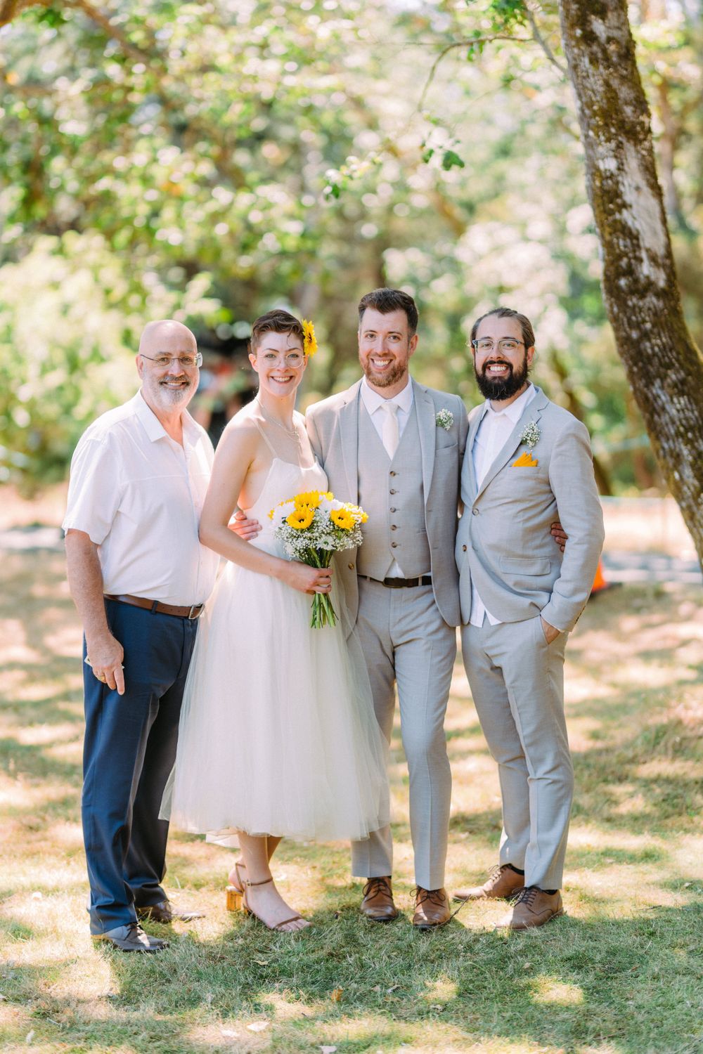 Wedding portrait of group standing under shaded trees in summer garden.