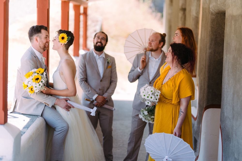 Wedding party gathers under parasols in covered outdoor venue by the sea.