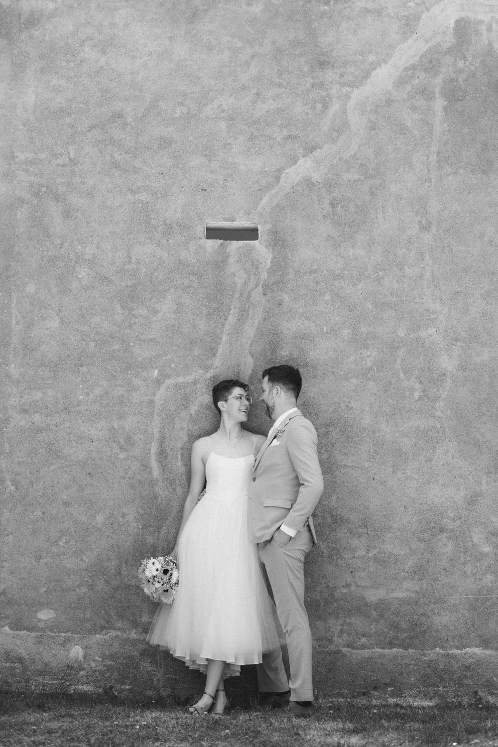 Black and white wedding portrait against textured wall with minimalist architectural detail.