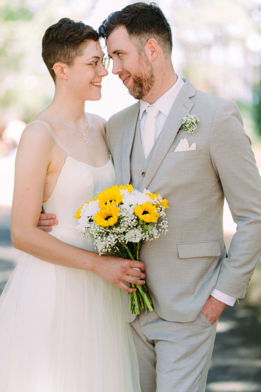 A romantic wedding portrait shows a couple sharing an intimate moment with yellow sunflowers and baby's breath bouquet.