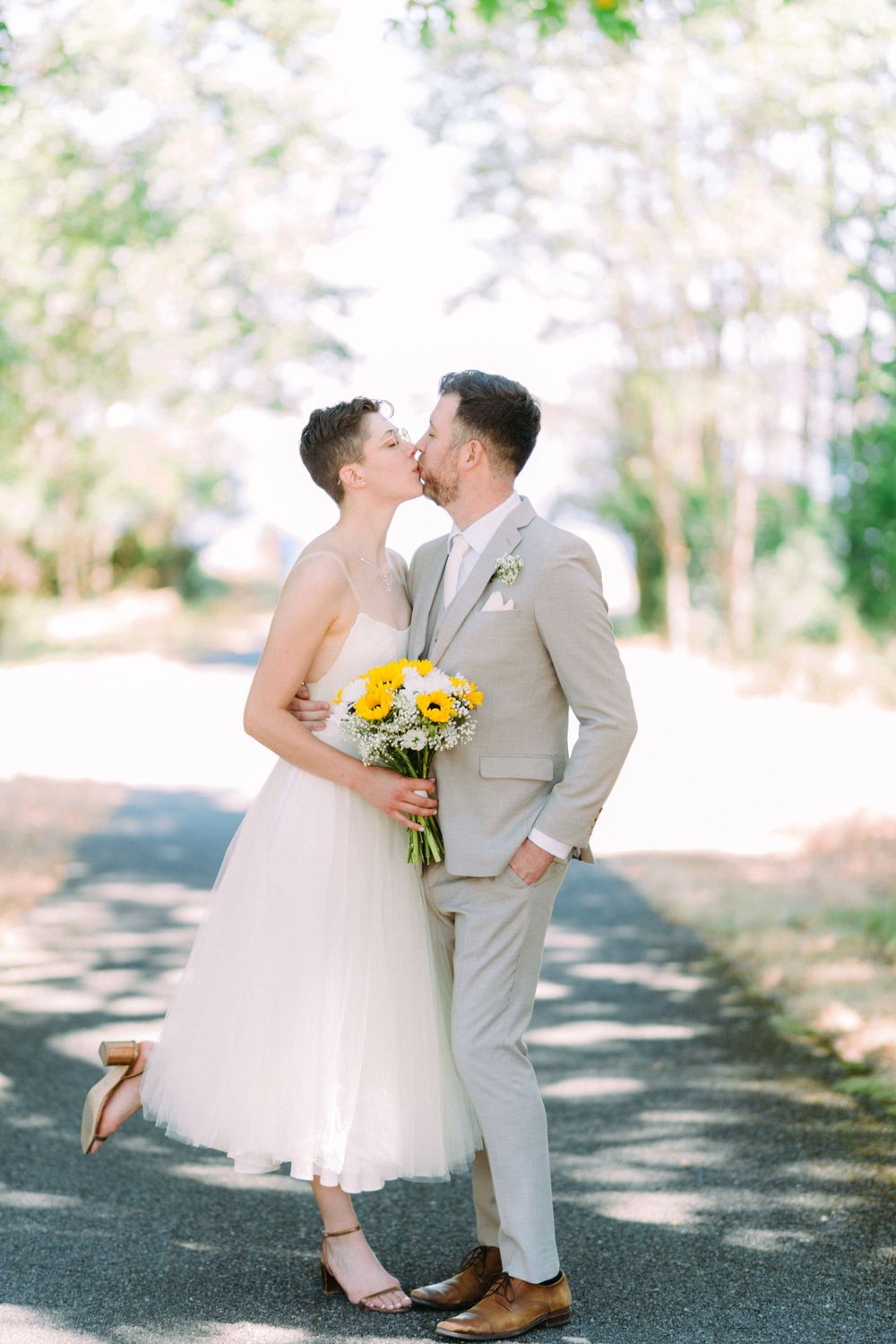 A tender wedding moment captured on a tree-lined path with the couple sharing a kiss.