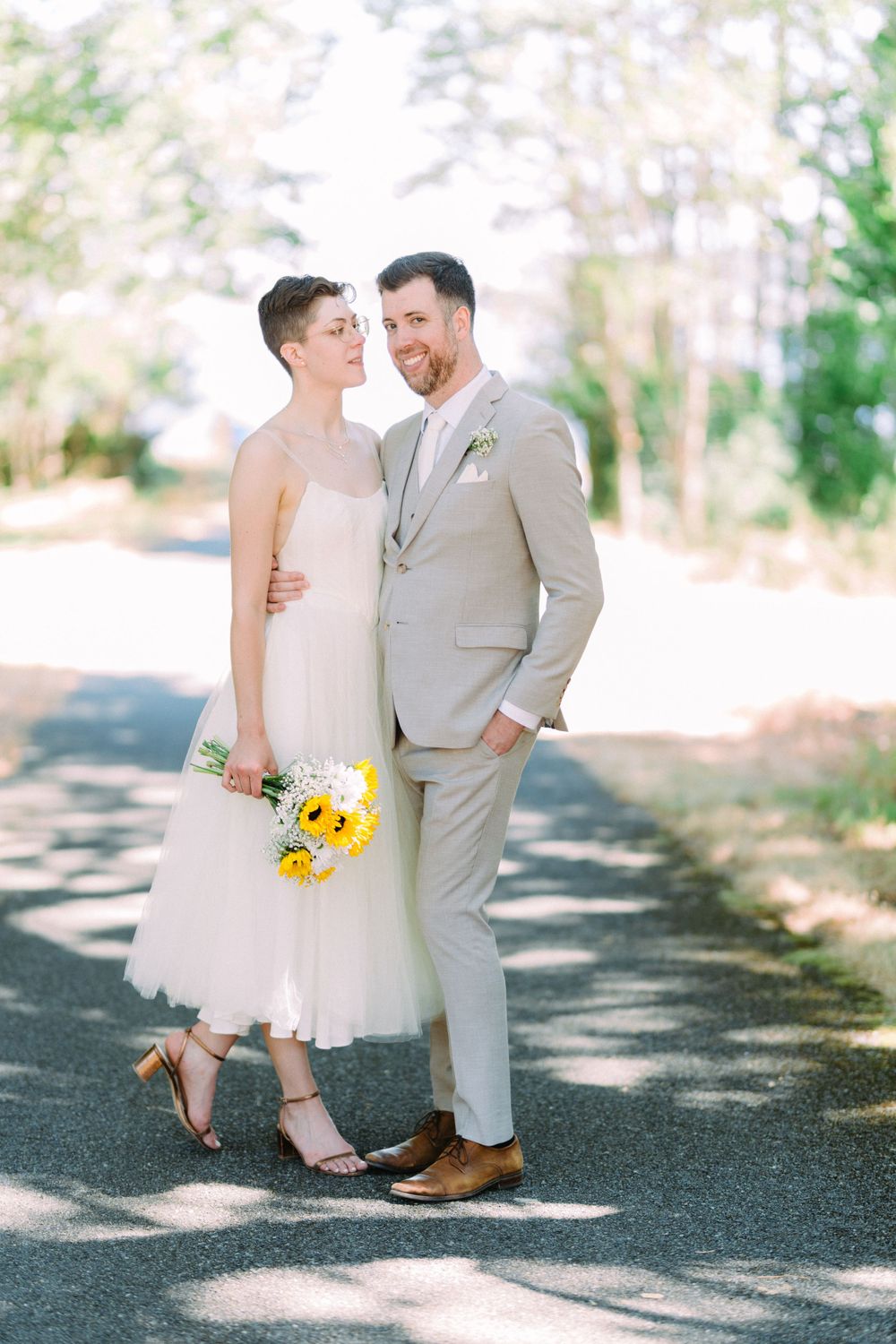 A candid wedding photo shows the couple laughing together on a sunlit forest path.