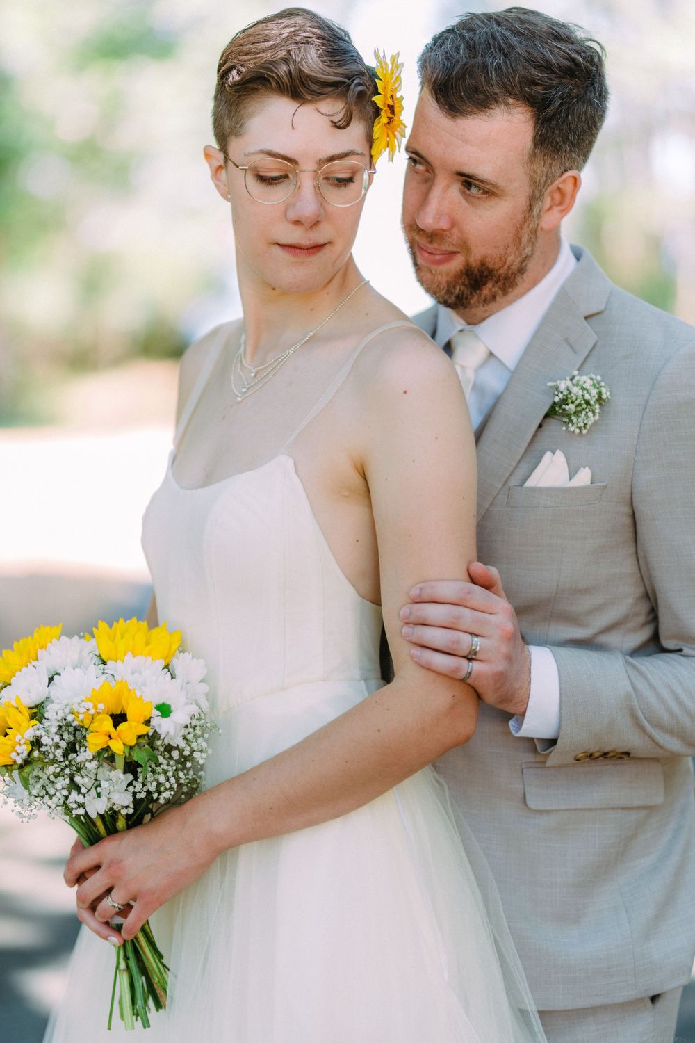 An artistic wedding portrait features a bouquet of sunflowers and white flowers in soft natural light.