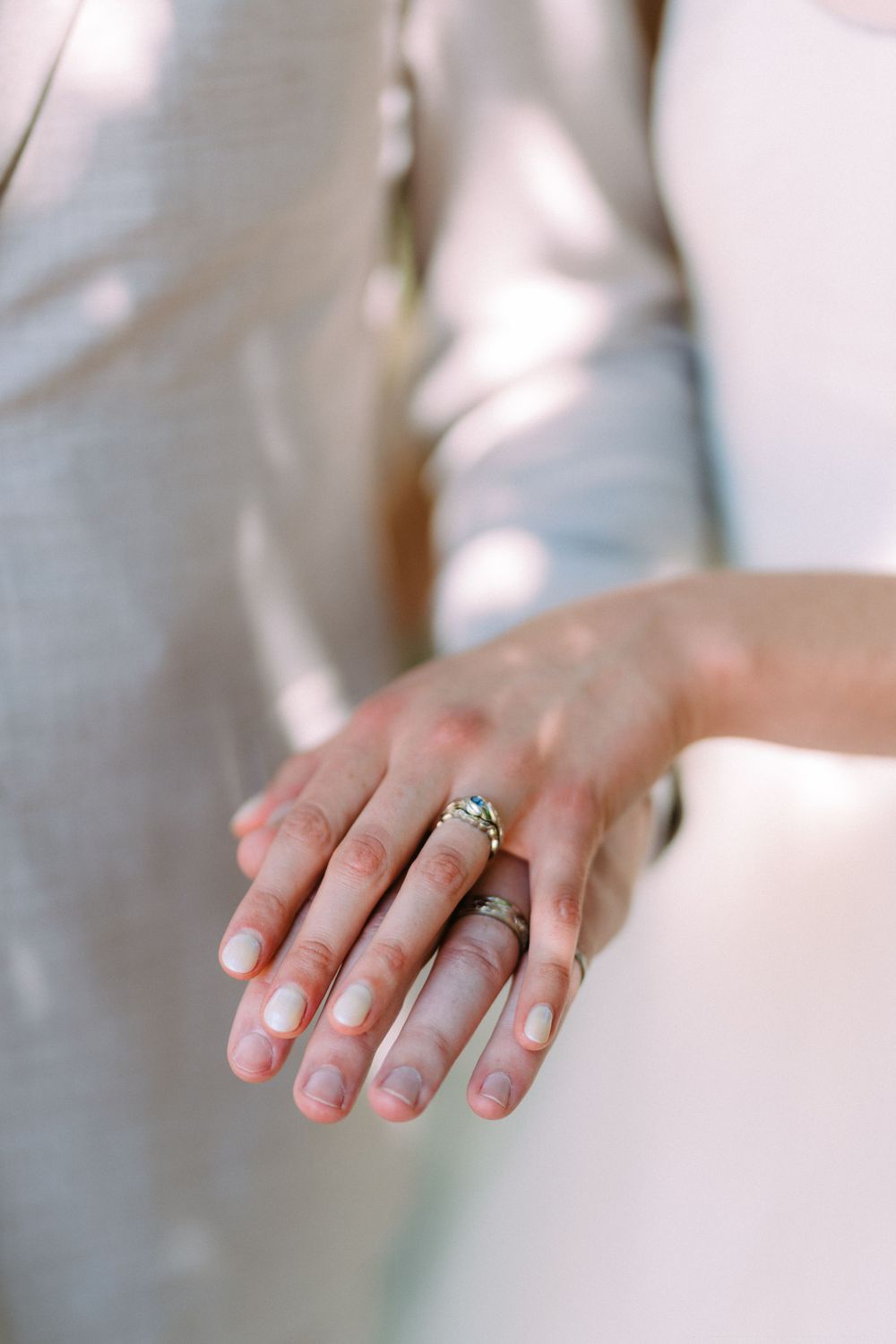 A close-up shot of wedding rings and clasped hands shows delicate jewelry details.