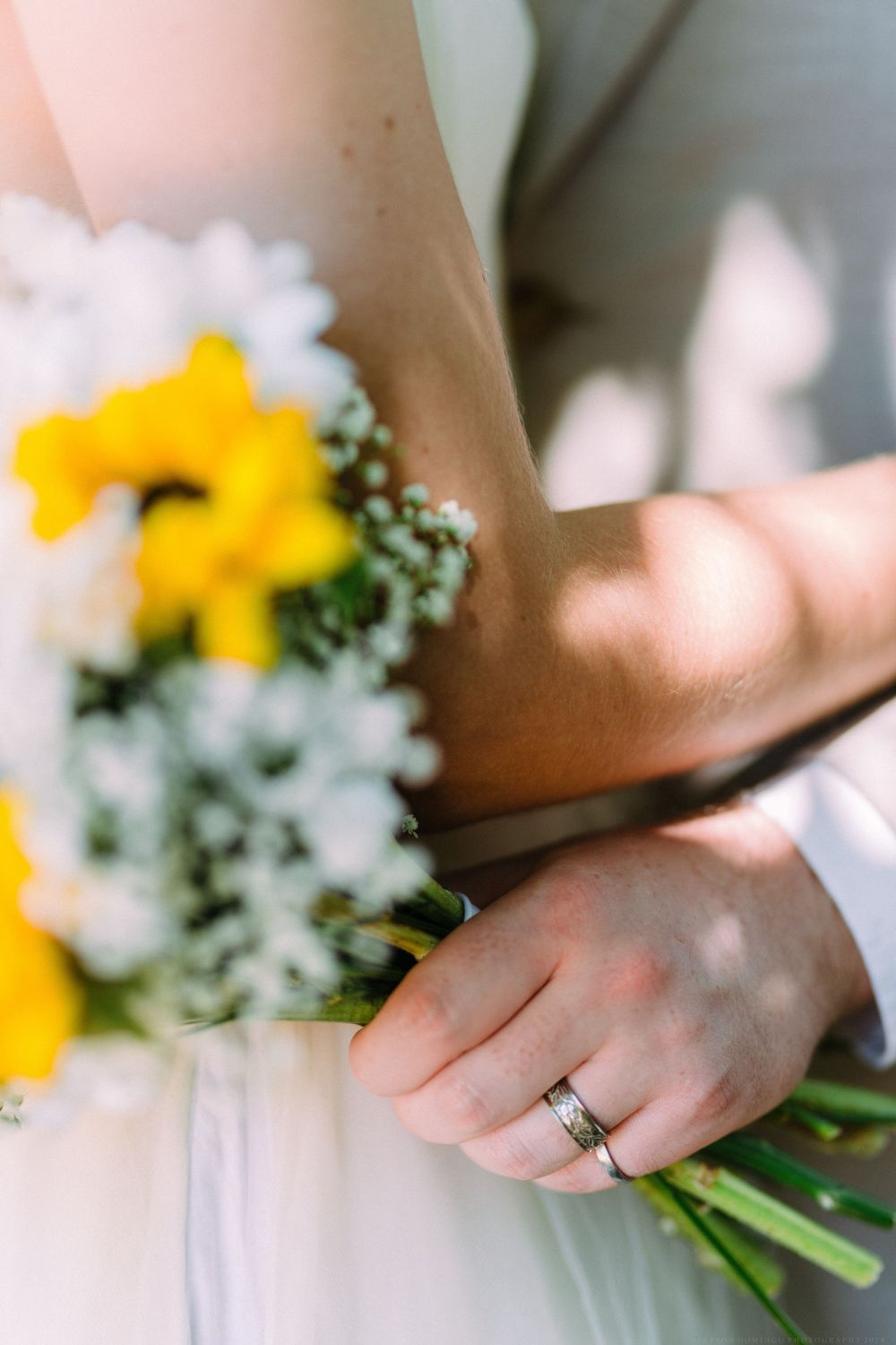 A detail shot of wedding rings with yellow sunflowers and white flowers in soft focus.