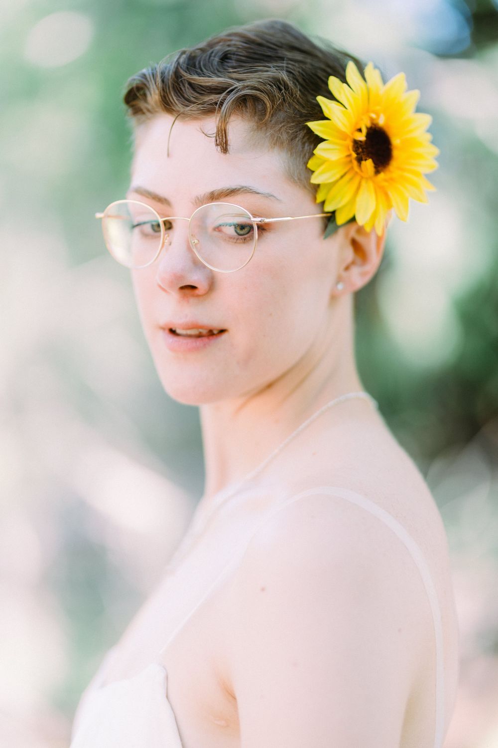 Ethereal portrait featuring a white dress and vibrant sunflower accessory against a soft bokeh background.