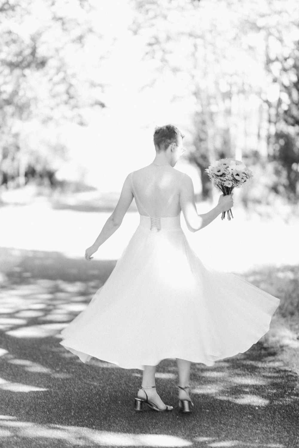 Black and white photo of a twirling bride in a tea-length dress holding a bouquet.