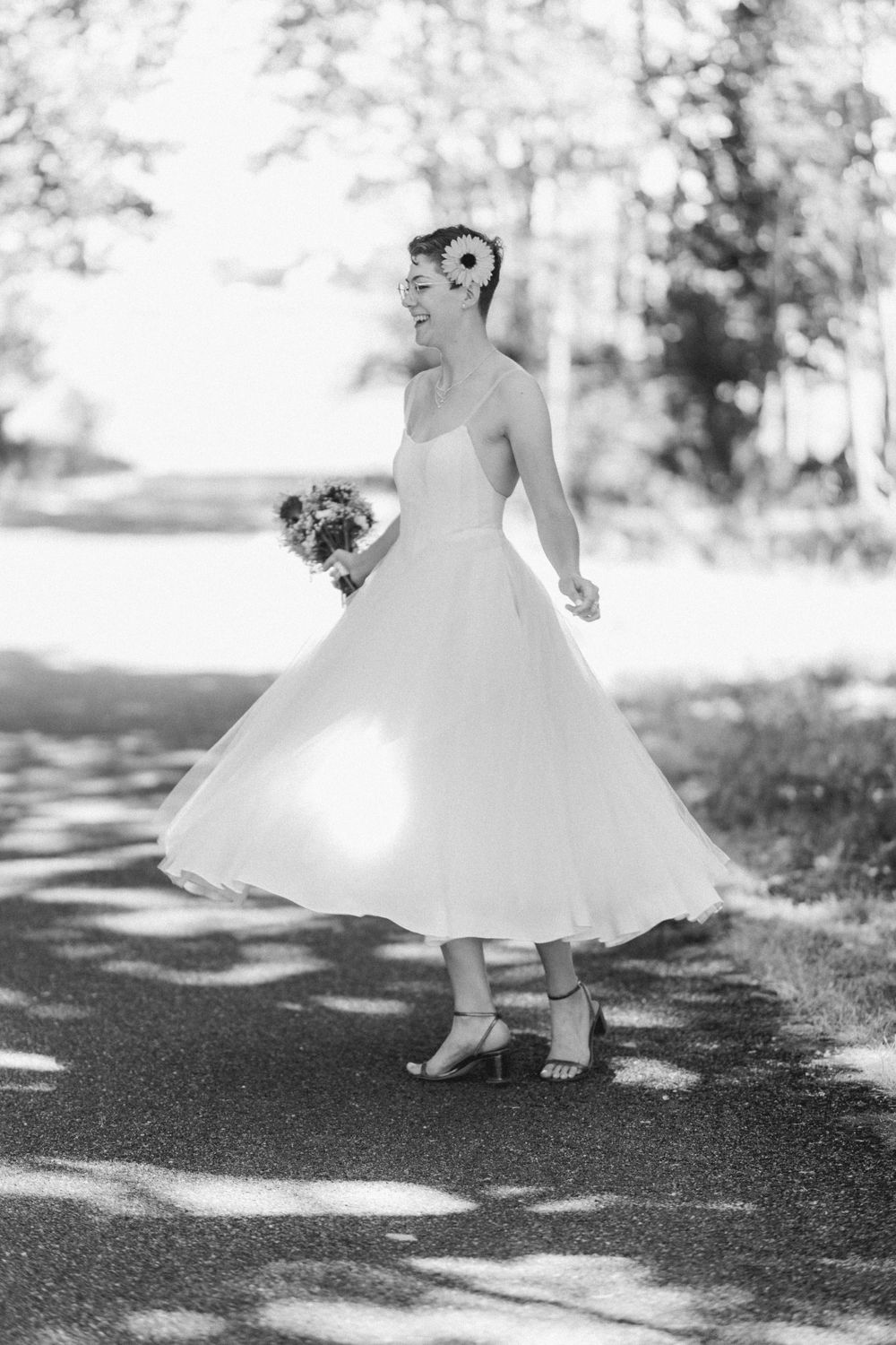 Black and white photograph capturing a joyful twirl in a tea-length wedding dress.