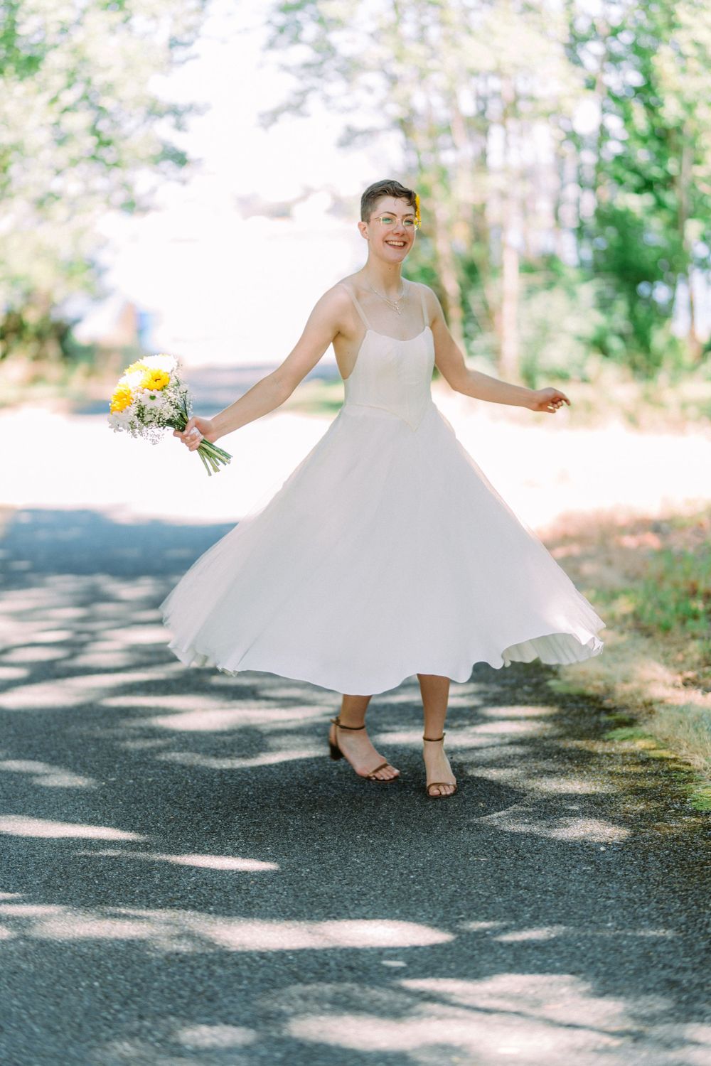 Sun-dappled portrait of a spinning bride in a vintage-inspired dress holding sunflowers.
