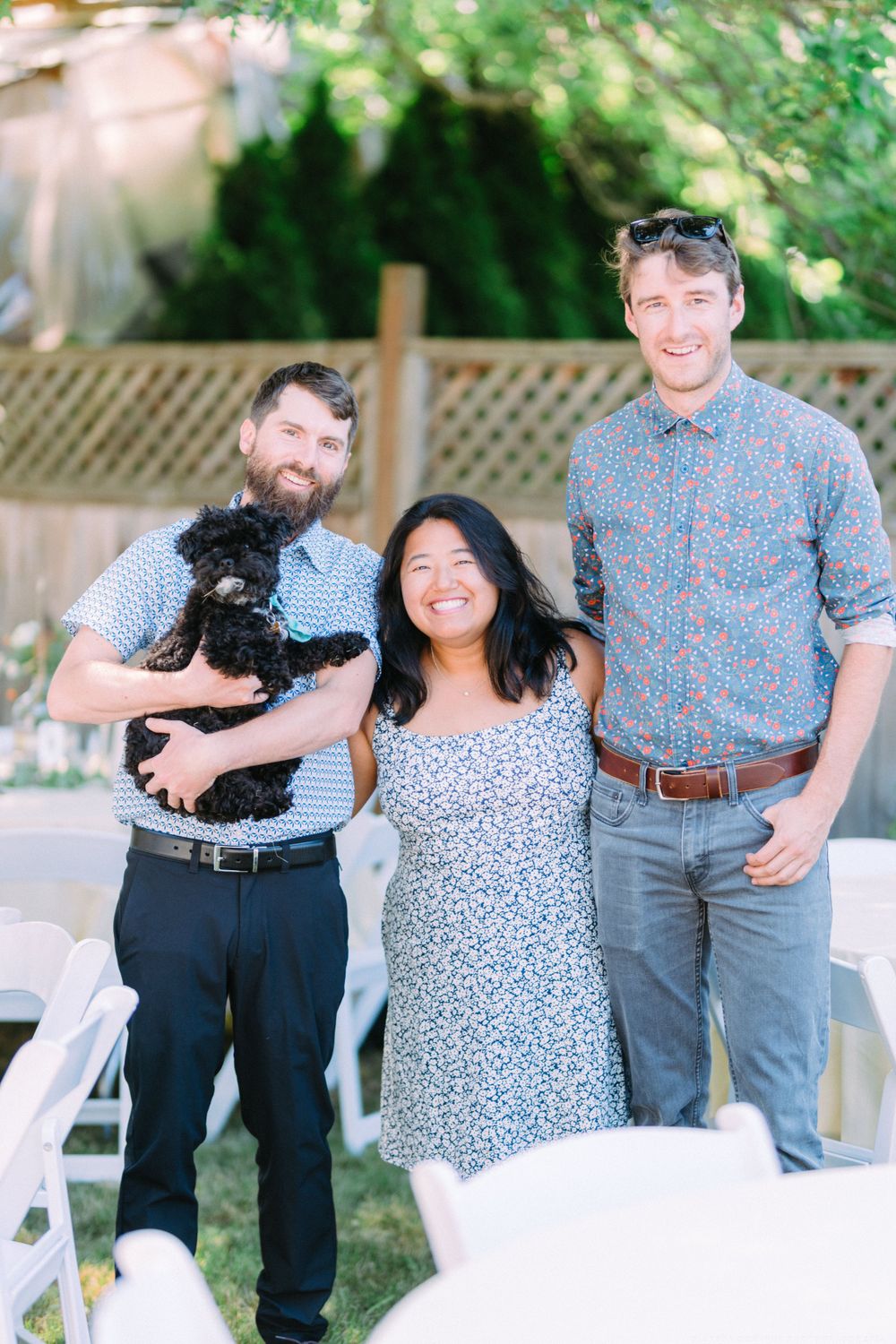 Casual outdoor gathering with three people and a small black dog at a backyard event.