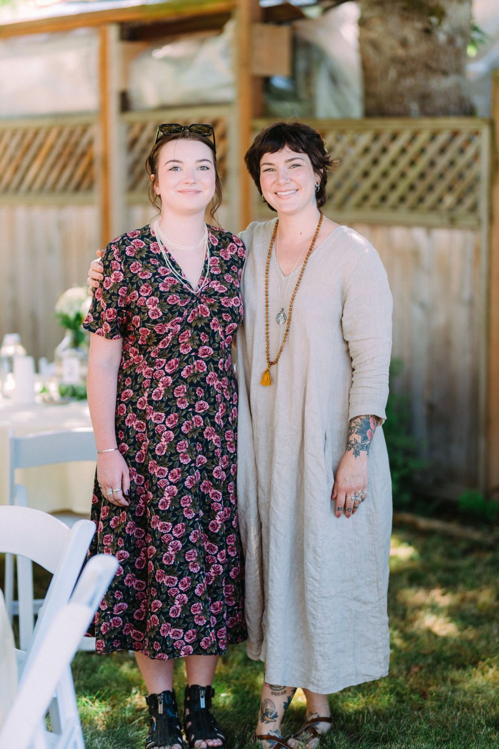 Two people in floral and neutral dresses standing together at an outdoor event.