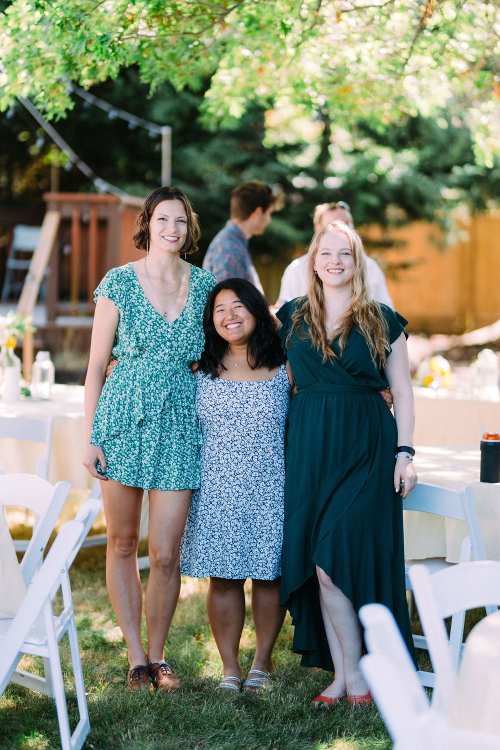 Three wedding guests in patterned dresses standing together at outdoor reception.