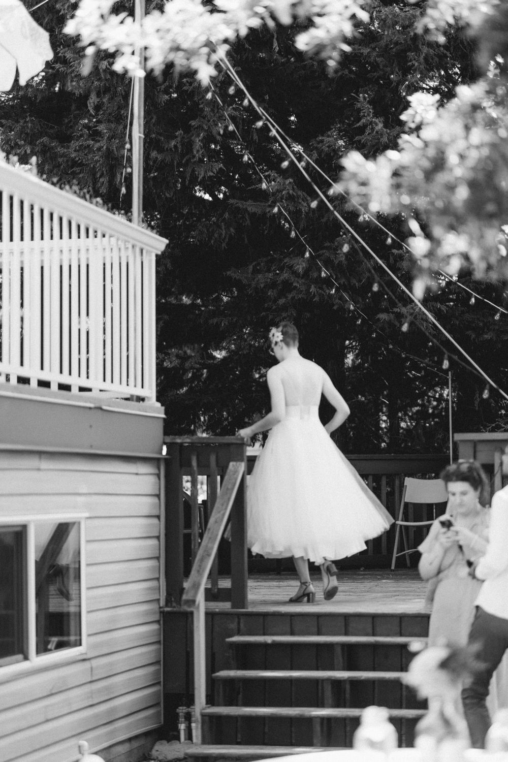 Black and white photo of person in wedding dress standing on outdoor deck stairs.