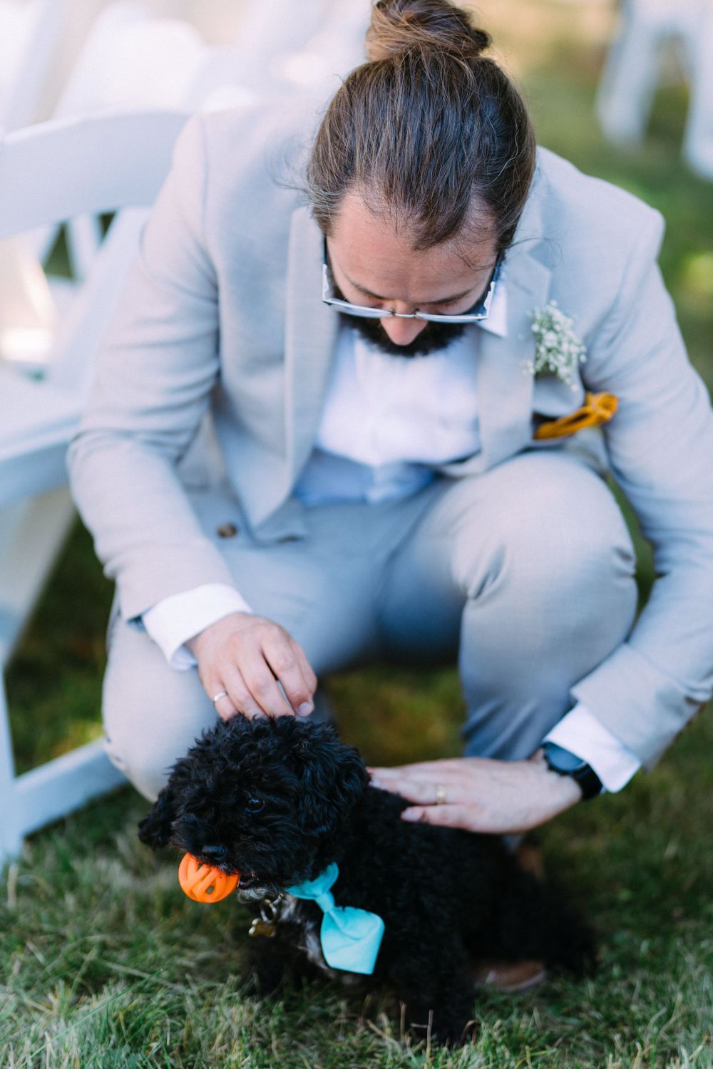 A black dog wearing a turquoise bandana being petted at an outdoor event.