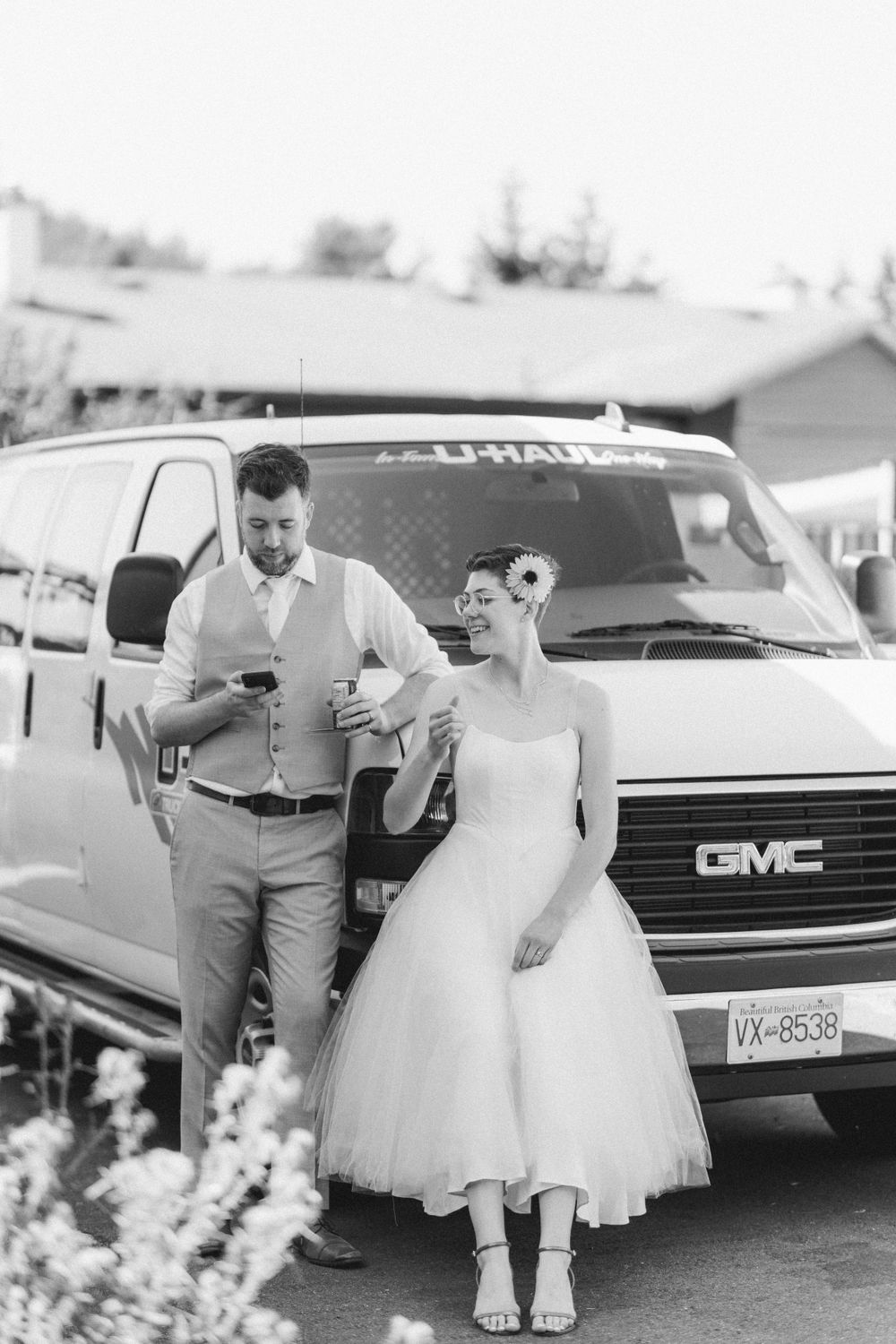 Black and white photo of a couple standing next to a GMC van in casual wedding attire.