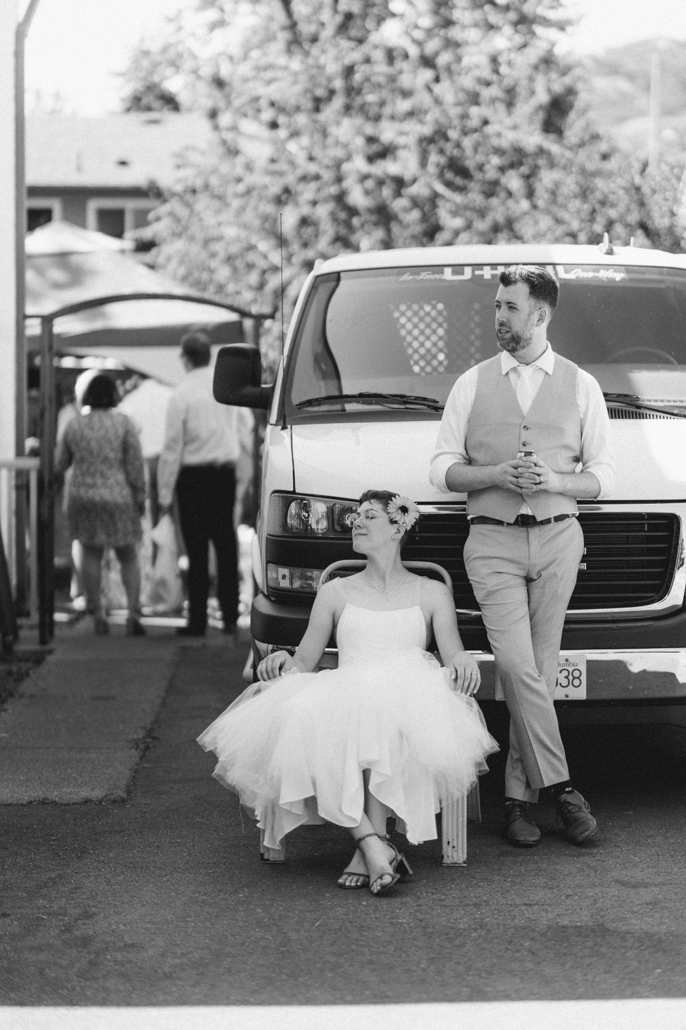 Black and white photo of a couple posing beside a parked van on a street.