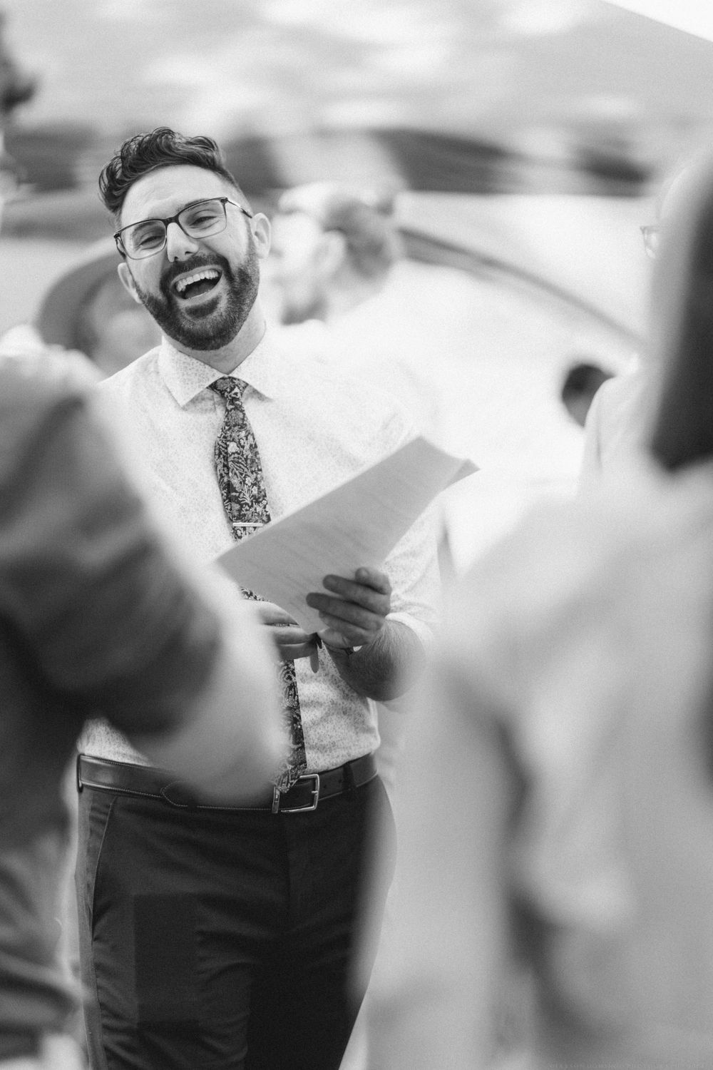 Black and white photo of someone laughing while holding papers at an outdoor event.