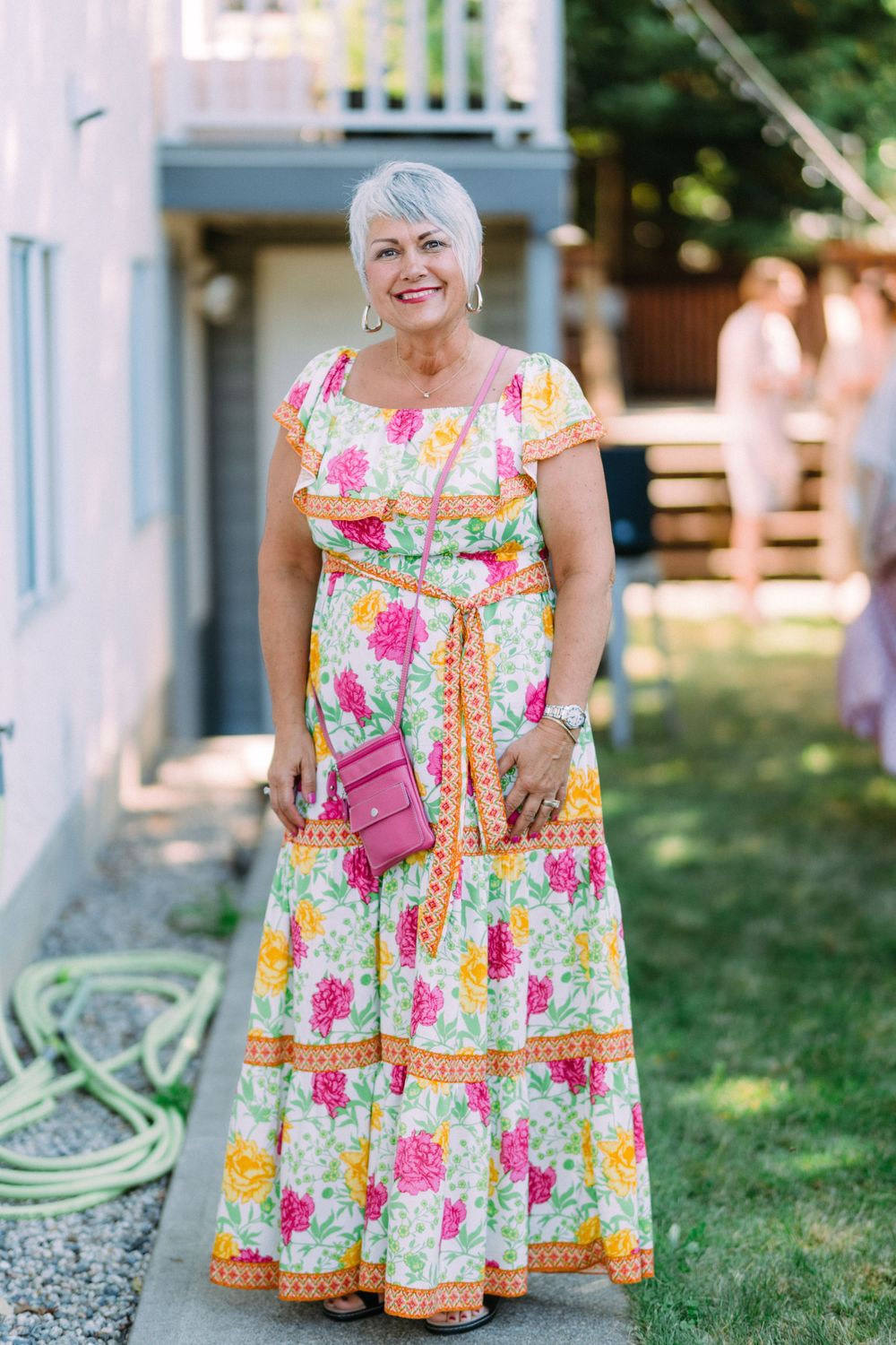 Woman in a colorful floral maxi dress standing in front of a white house.