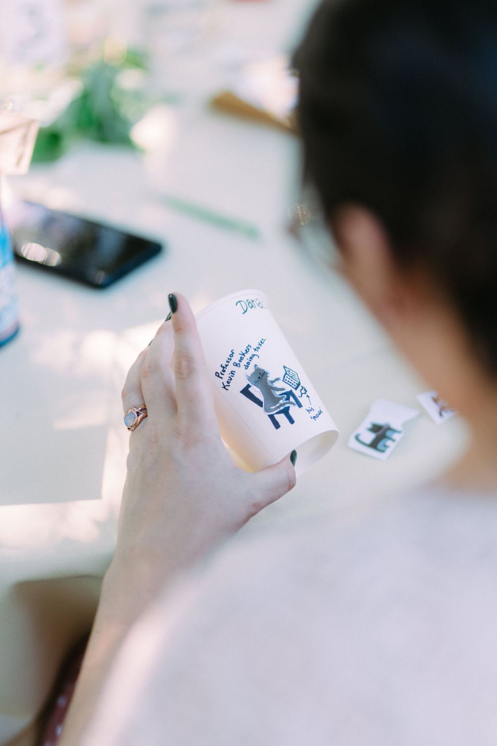 Close-up of hands holding a decorative paper cup at an outdoor event.