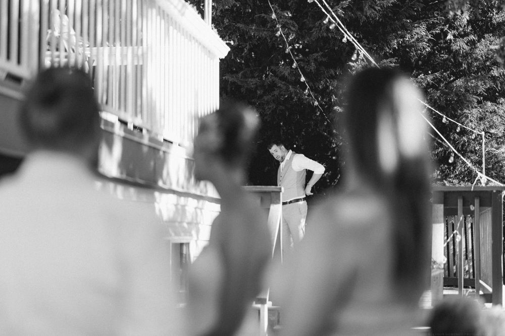 A soft focus black and white wedding ceremony photo showing silhouetted guests watching at an outdoor venue.