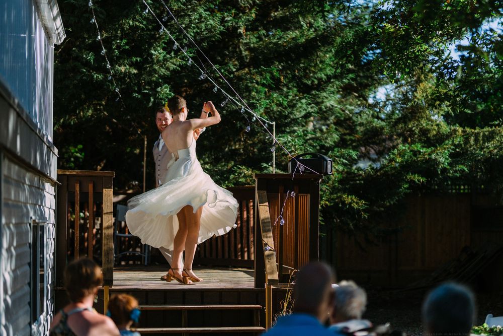 A bride in a tea-length dress twirls during an outdoor wedding dance performance.