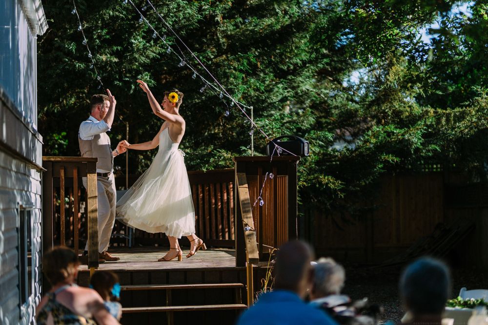 A couple performs a choreographed dance on an outdoor wooden deck while guests watch below.