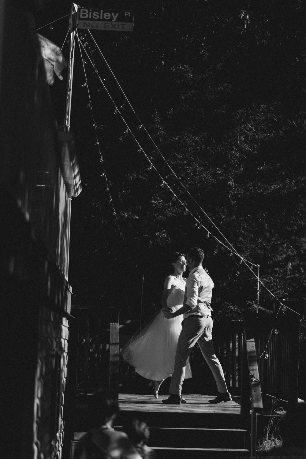 A black and white photo captures a couple's romantic dance moment on an outdoor deck.