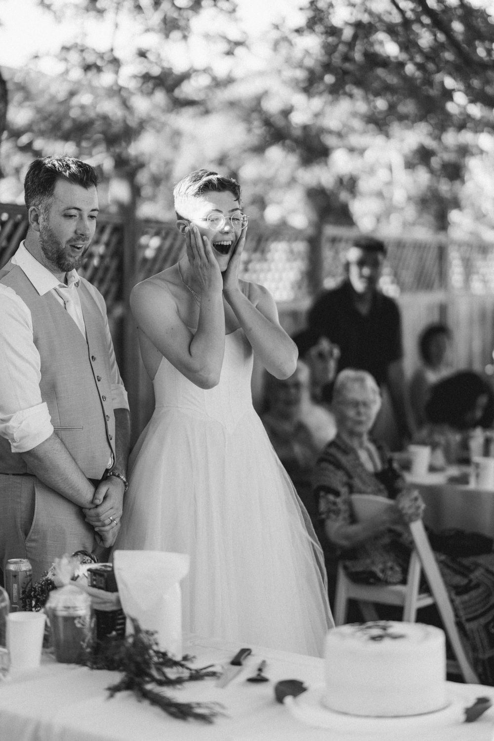 A candid black and white moment of joy at a wedding reception table with cake.