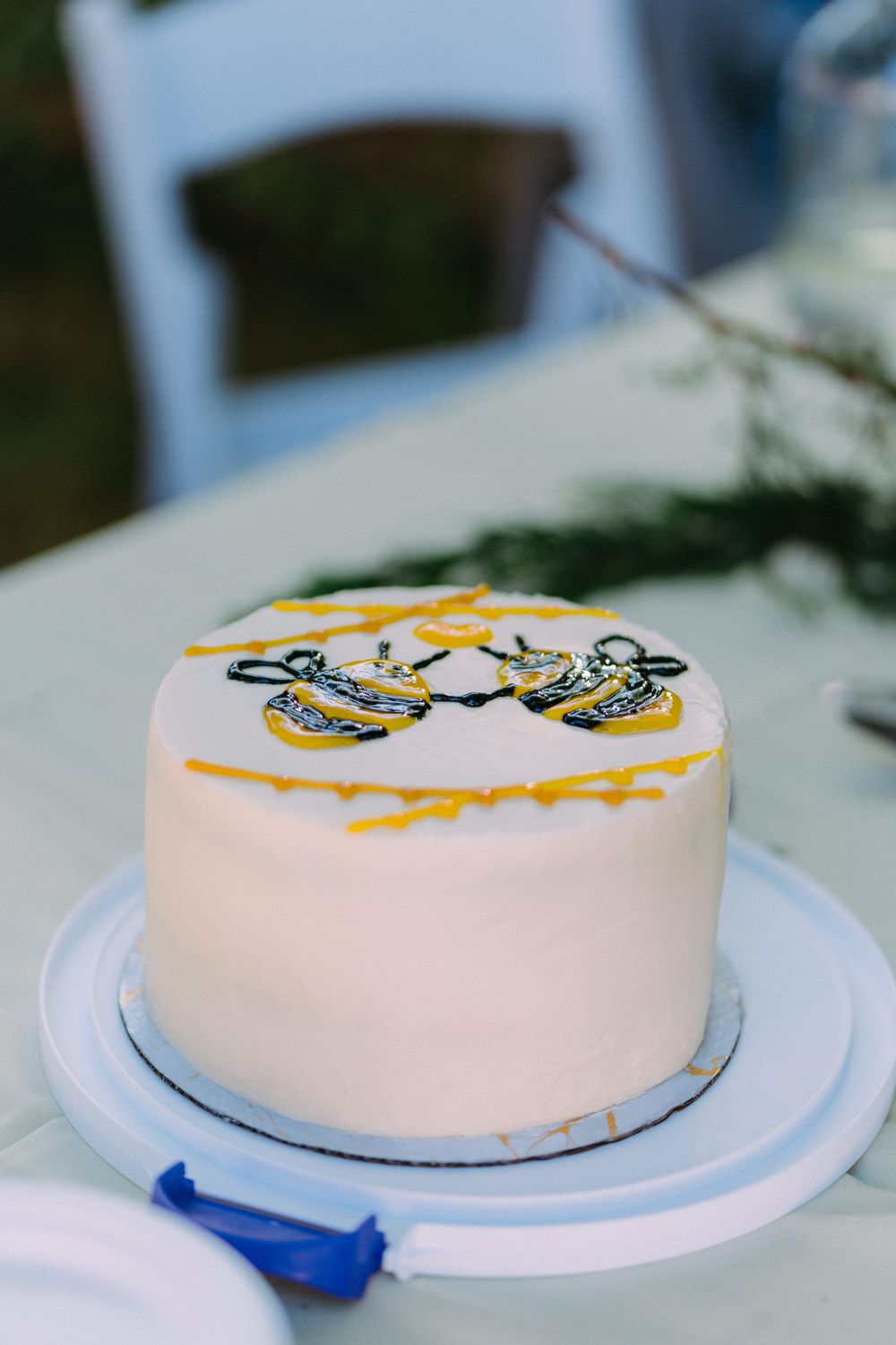 A white frosted cake decorated with yellow and black bumblebee designs on top, displayed on a white cake stand.