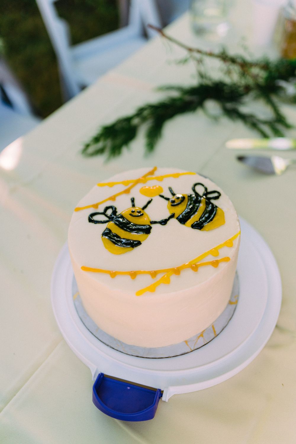 Small white cake decorated with yellow and black bumblebee designs and honey drips on a round cake plate.