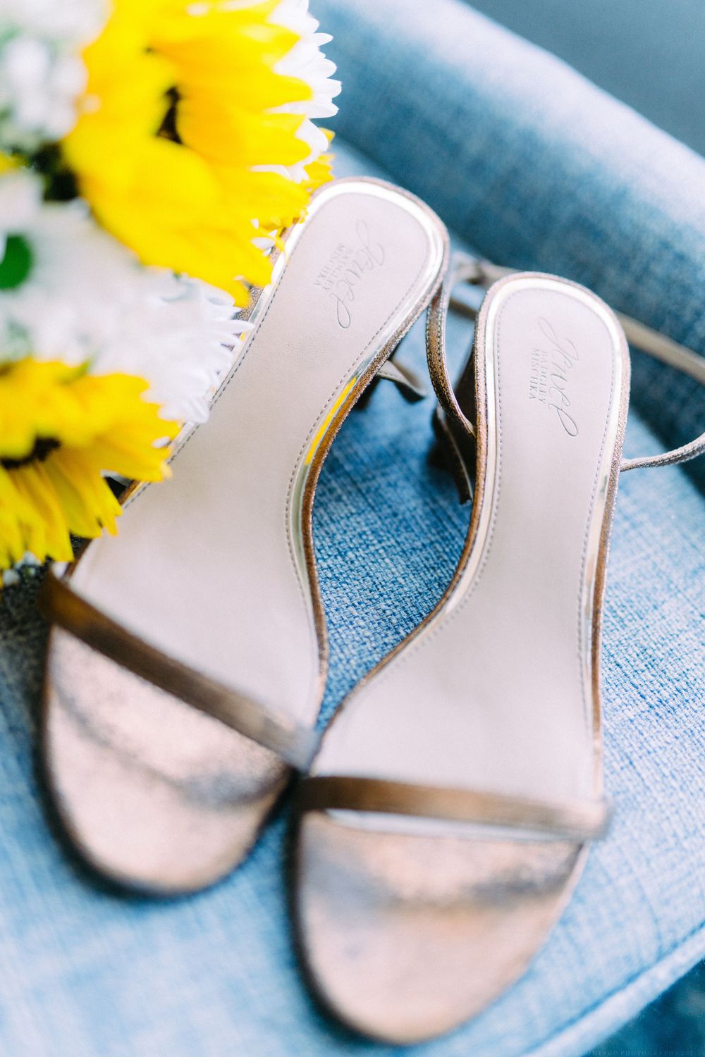 Elegant metallic bridal sandals displayed with bright sunflowers on blue fabric.