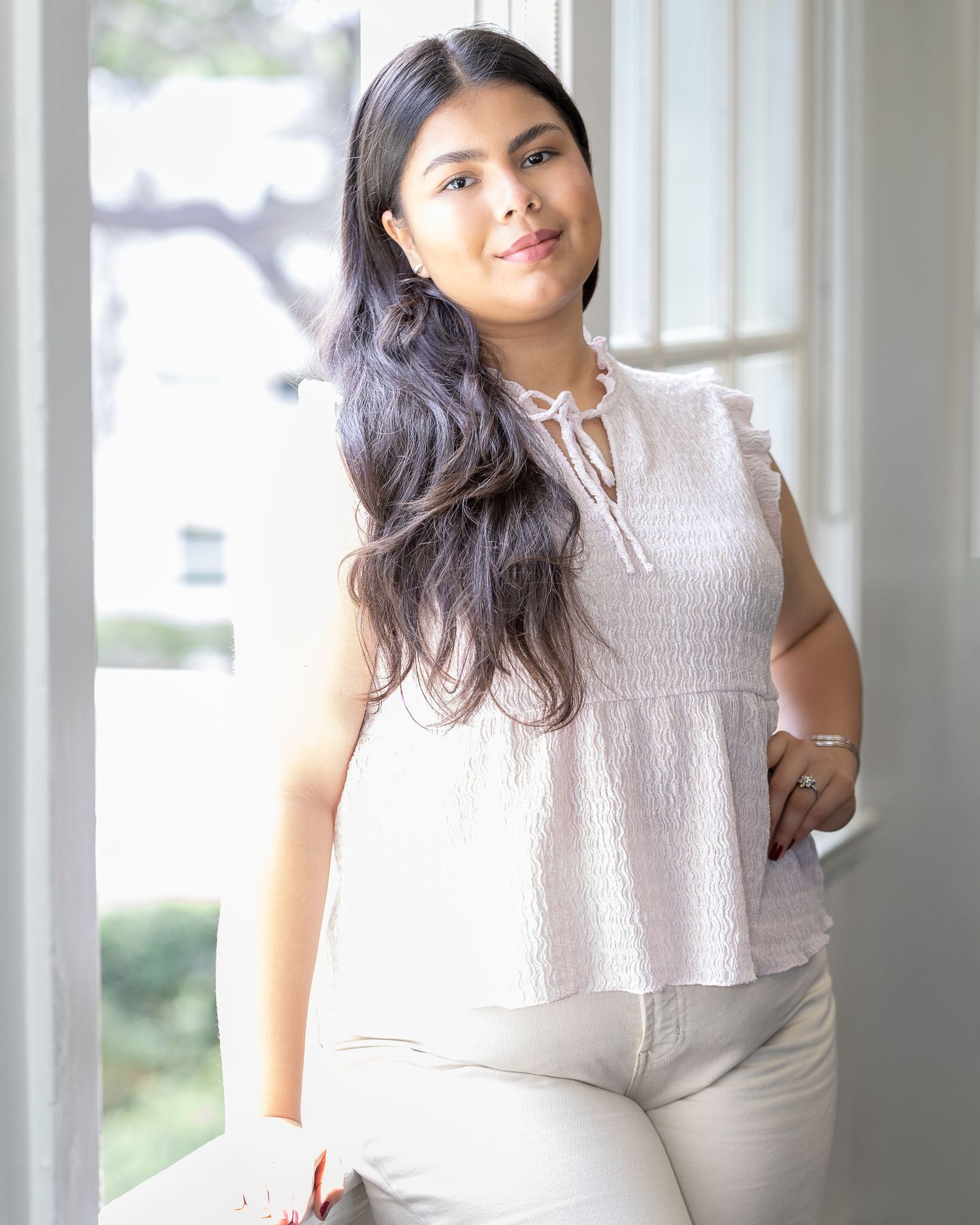 Female poses next to a window in a natural pose for a professional headshot. Professional photographer poses the model for a headshot.