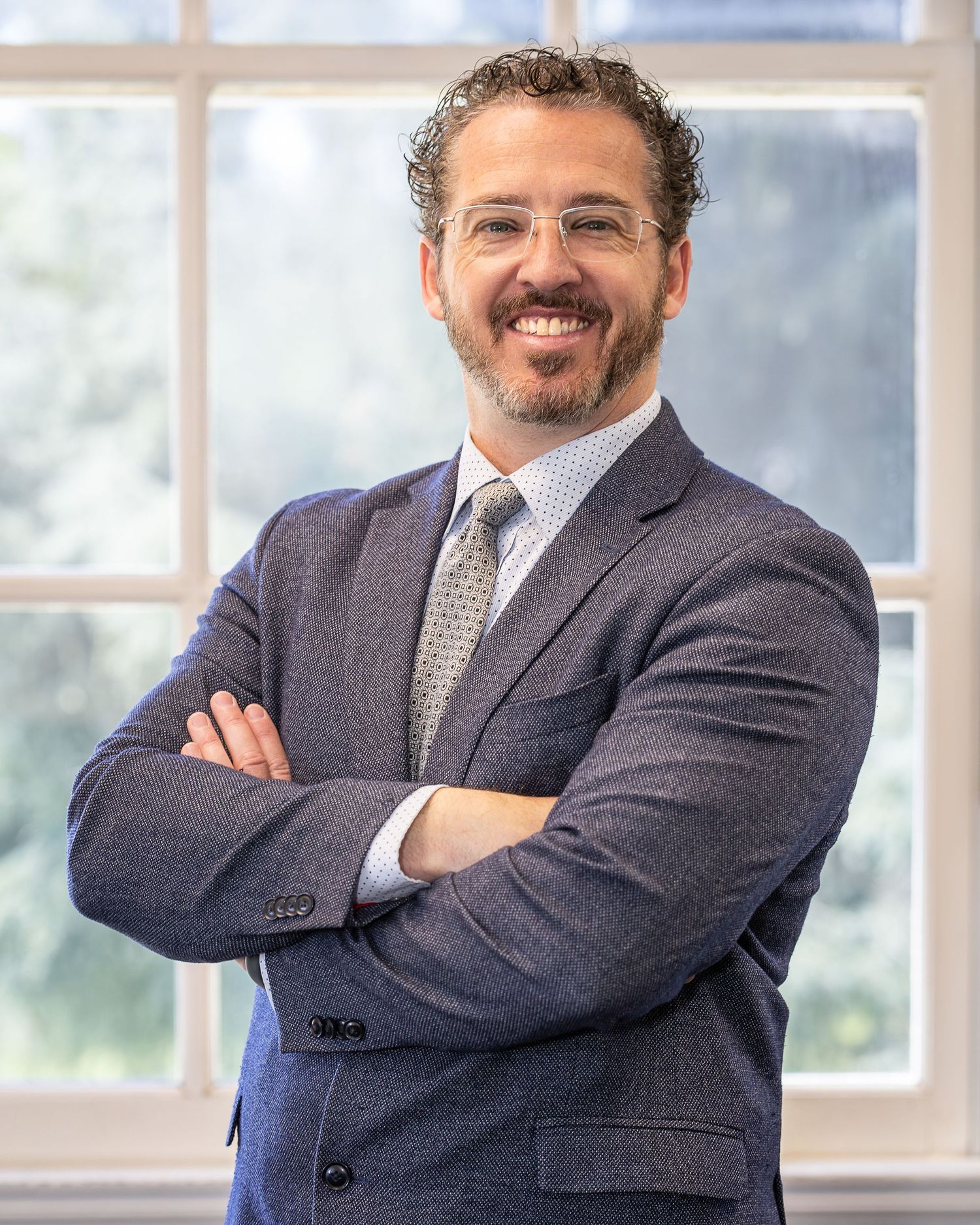 Male poses for Business Headshot. Male is wearing a blazer and poses for a professional portrait/headshot using natural light.