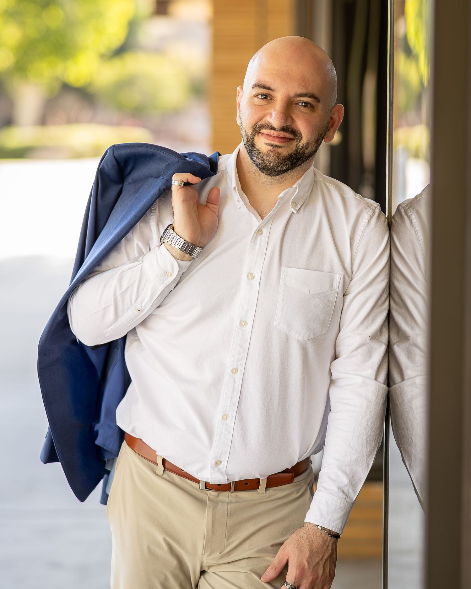 Professional headshot using natural light. Male poses for a headshot wearing business casual clothing with a blazer over his shoulder.