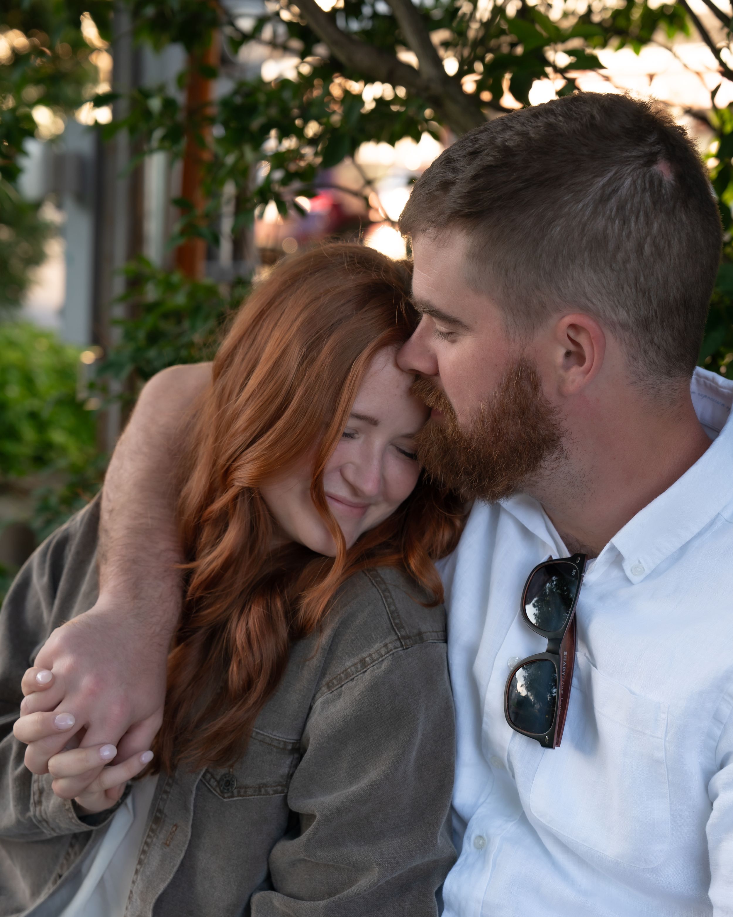 Engaged couple outside Hare of the Dawg bar in Derry, NH, with the fiancé kissing his partner on the forehead during a c