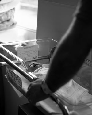 Father standing over hospital bassinet with newborn 24 hours after birth, captured by a Boston newborn photographer.