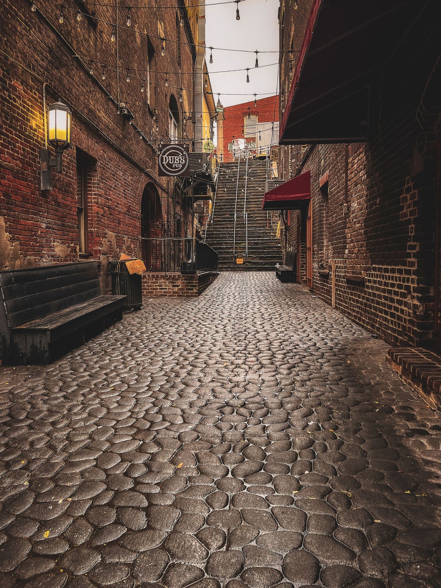 Historic cobblestone alley with brick walls and stone steps illuminated by vintage lanterns.