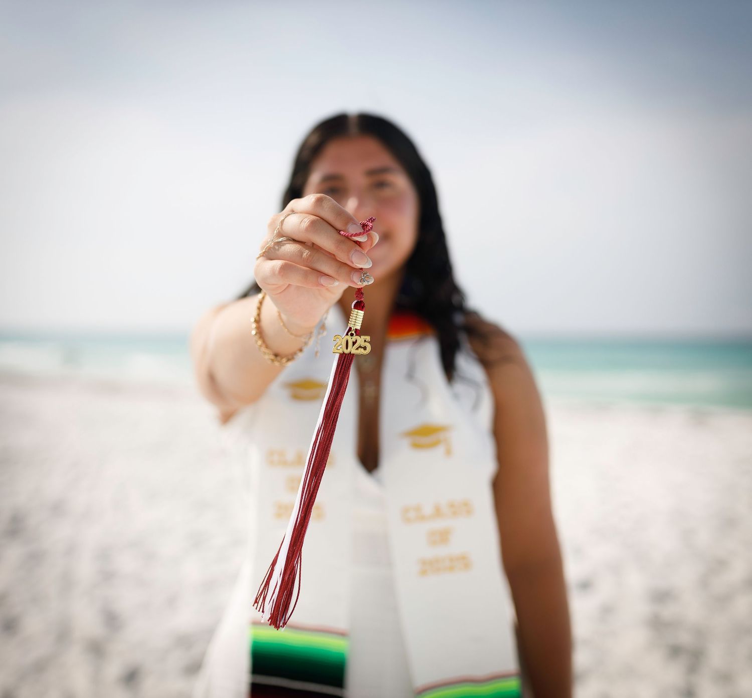 Hand holding up colorful tassel keychain against beach backdrop.