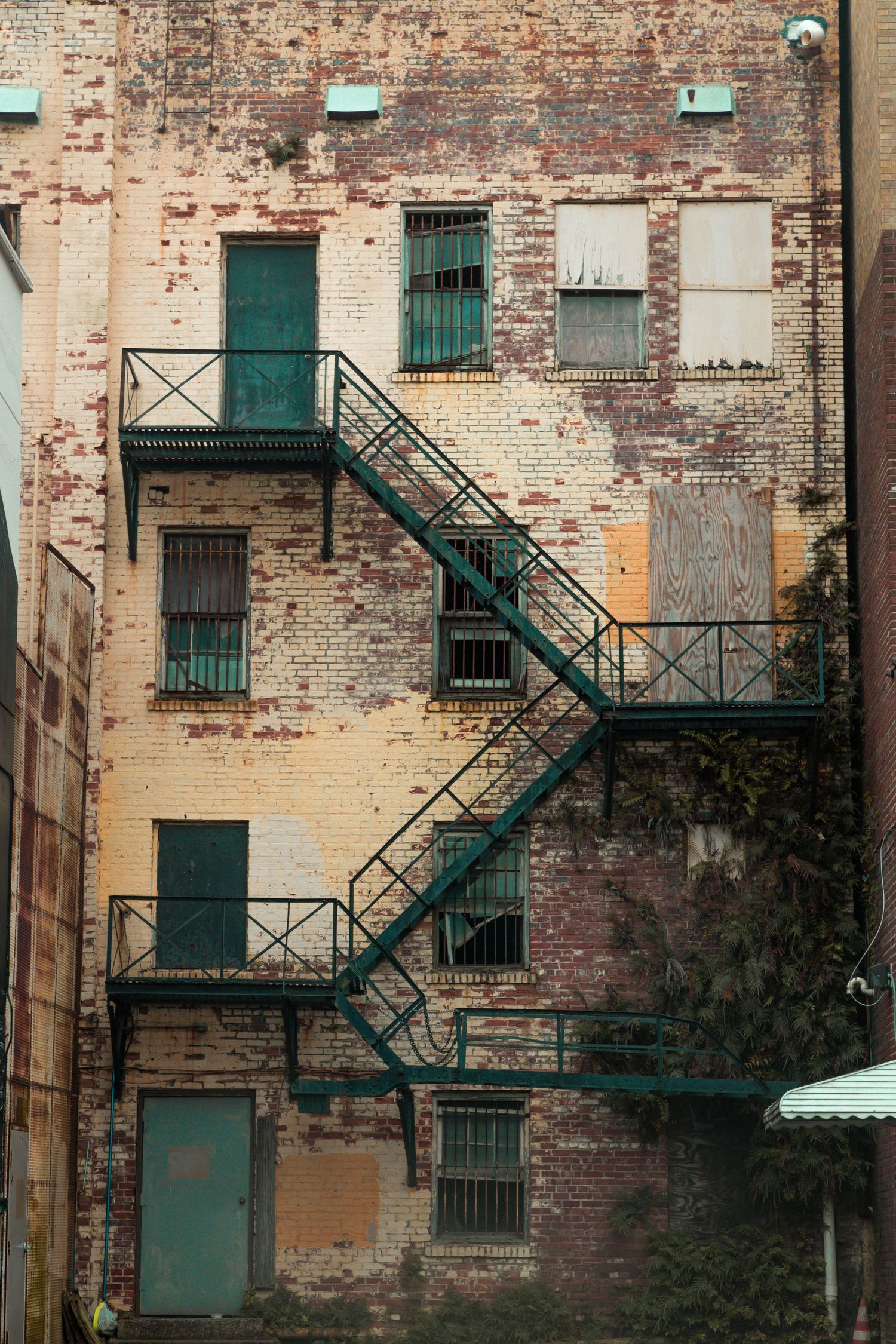 Rustic brick building facade with green fire escape stairs and weathered industrial windows.